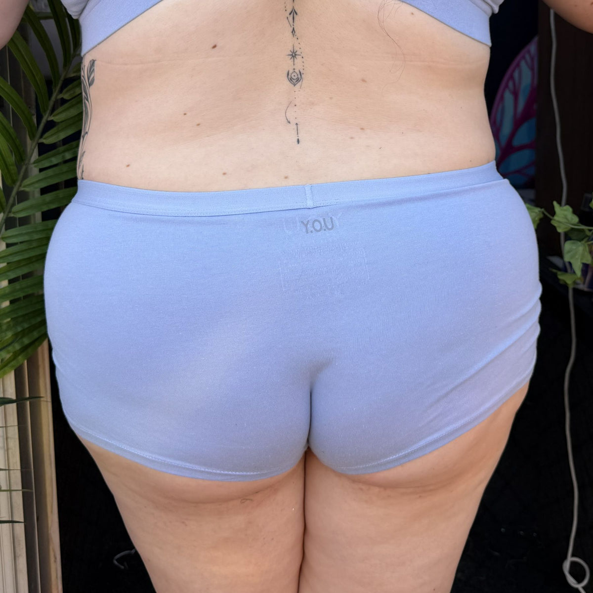 A photo of a model wearing the YOU Underwear boyshorts in light blue. They are standing, facing away from the camera. The photo is zoomed in so we can see from the model's mid-back to their upper-thigh.