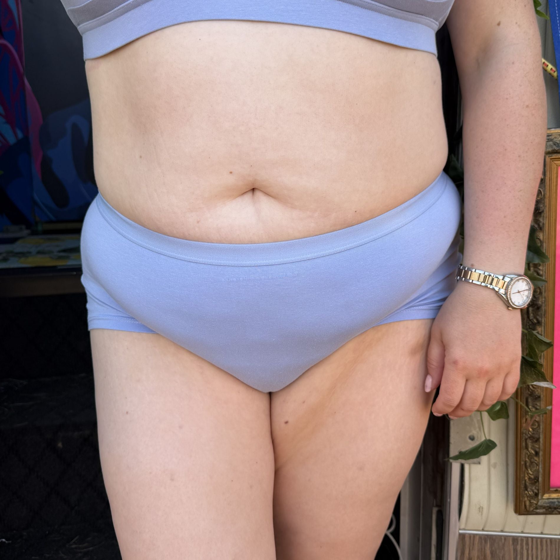 A photo of a model wearing the YOU Underwear boyshorts in light blue. The photo is zoomed in so we can see from the model's upper stomach to just above their knees. They are standing facing the camera, with their left arm at their side.