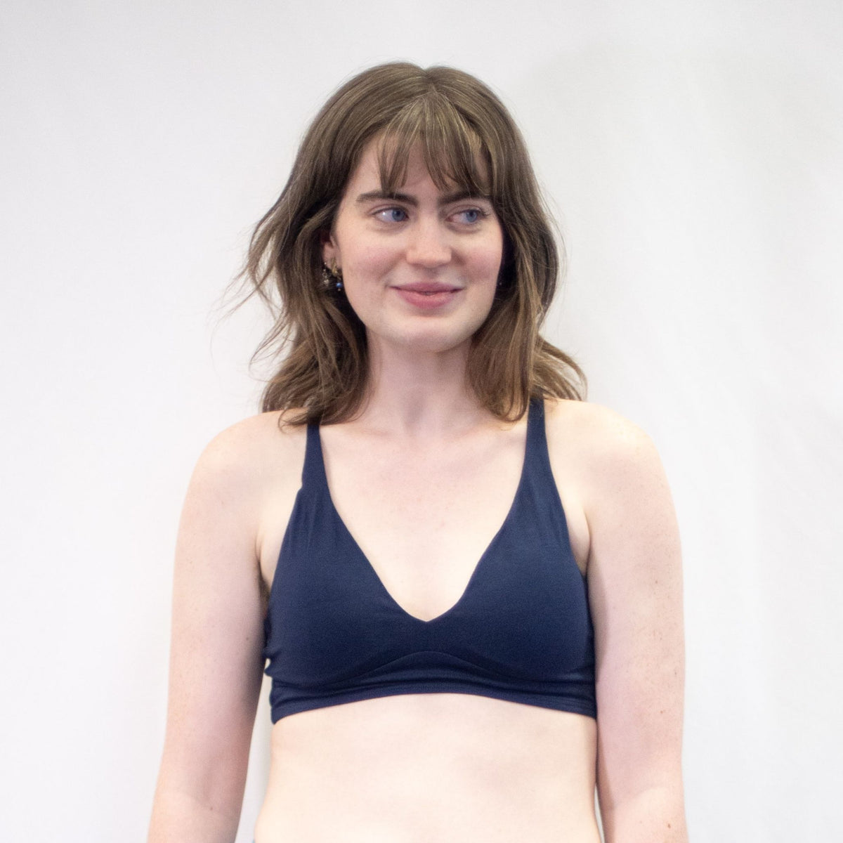 A photo of a model wearing the YOU Underwear padded bralette in navy blue. She is standing facing the camera with her hands at her sides, looking off to the left. There is a white background and the photo is cropped so we can see to the model's waist.