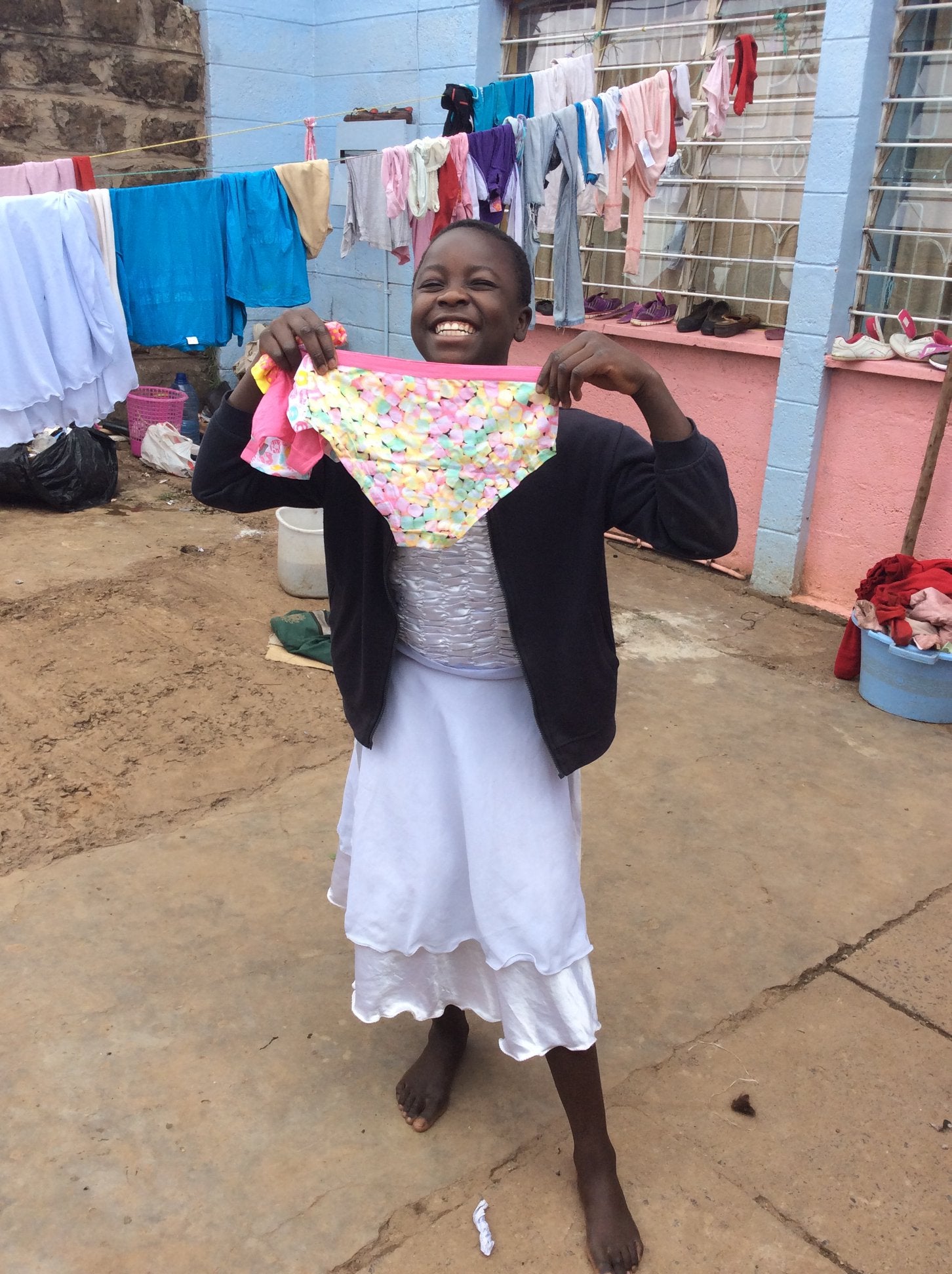 Girl in Uganda smiles as she holds up a pair of donated pants