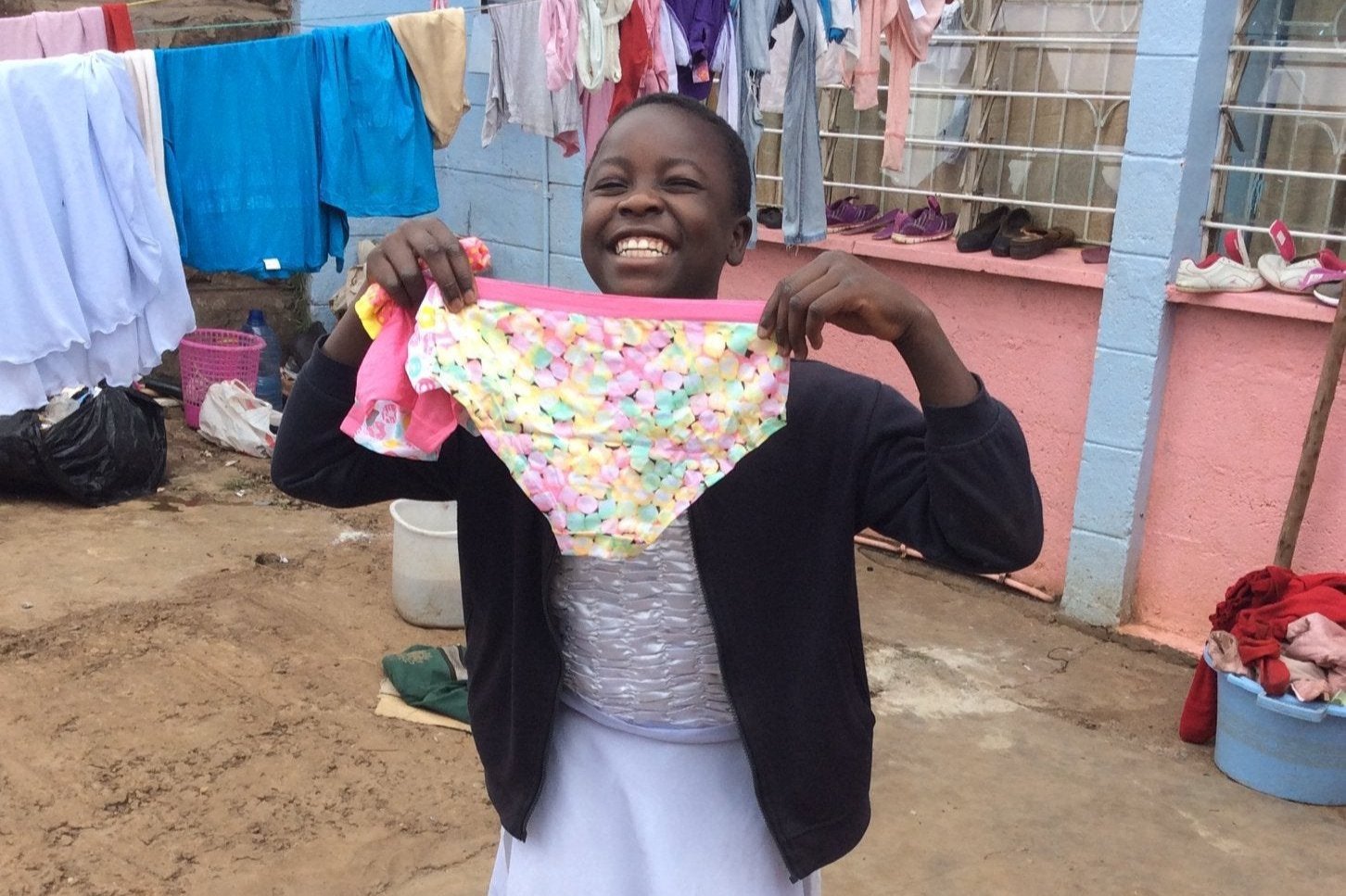 Girl in Uganda smiles as she holds up a pair of donated pants