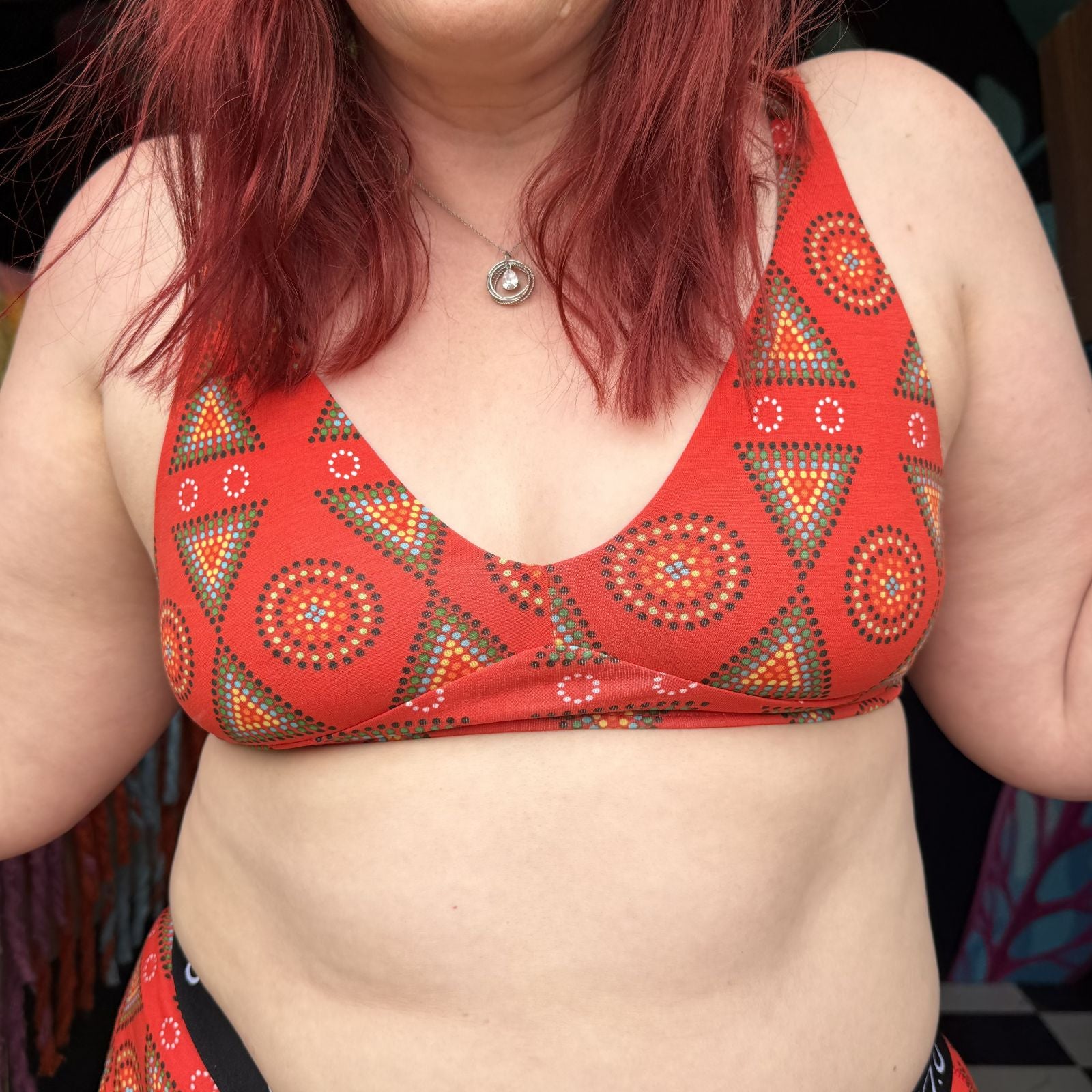 Photo of model wearing the YOU Underwear Bralette in Red Mara print. The model faces towards the camera, and the image is cropped from the chin to mid-stomach.