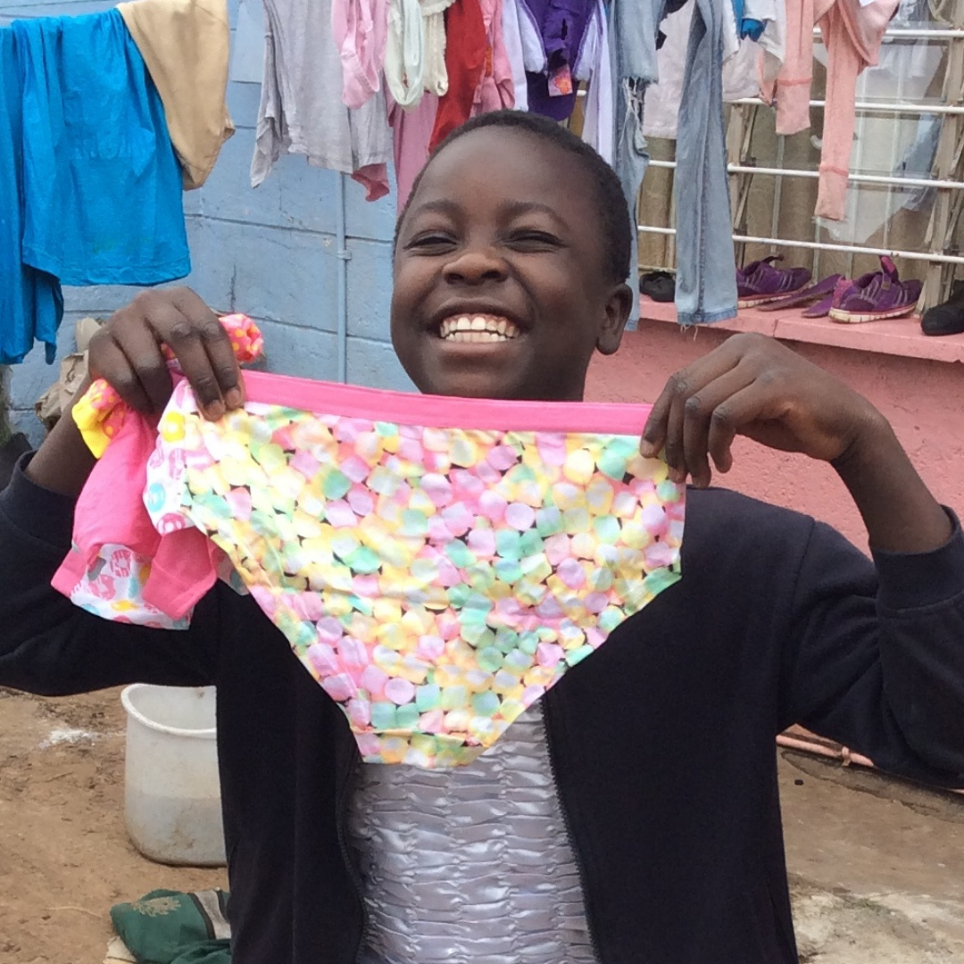 A young girl smiles whilst holding a brightly coloured pair of pants