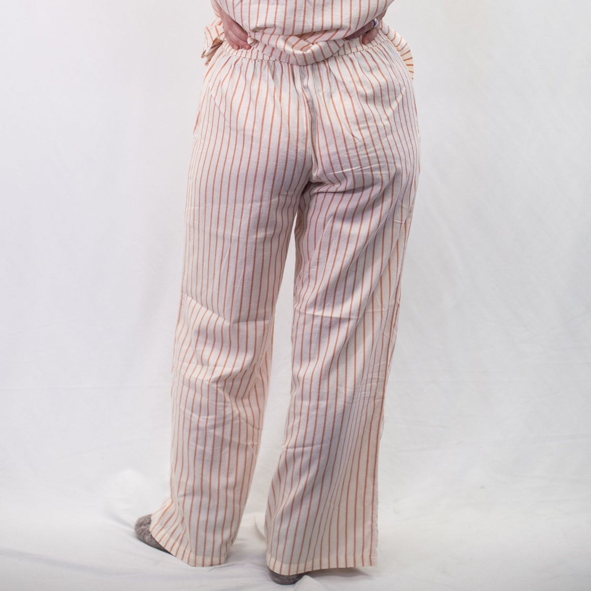 A photo of a model wearing the YOU Underwear woven pyjama bottoms in soft cream and coral. The photo is zoomed in so we can see from the model's stomach to the floor. They are facing away from the camera and there is a white background.