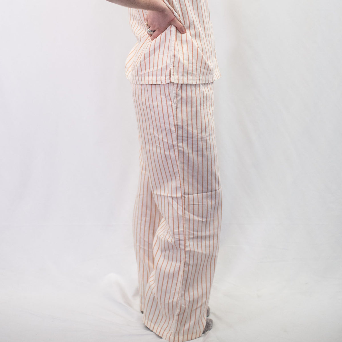 A photo of a model wearing the YOU Underwear woven pyjama bottoms in soft cream and coral. The photo is zoomed in so we can see from the model's stomach to the floor. They are side on to the camera and there is a white background.