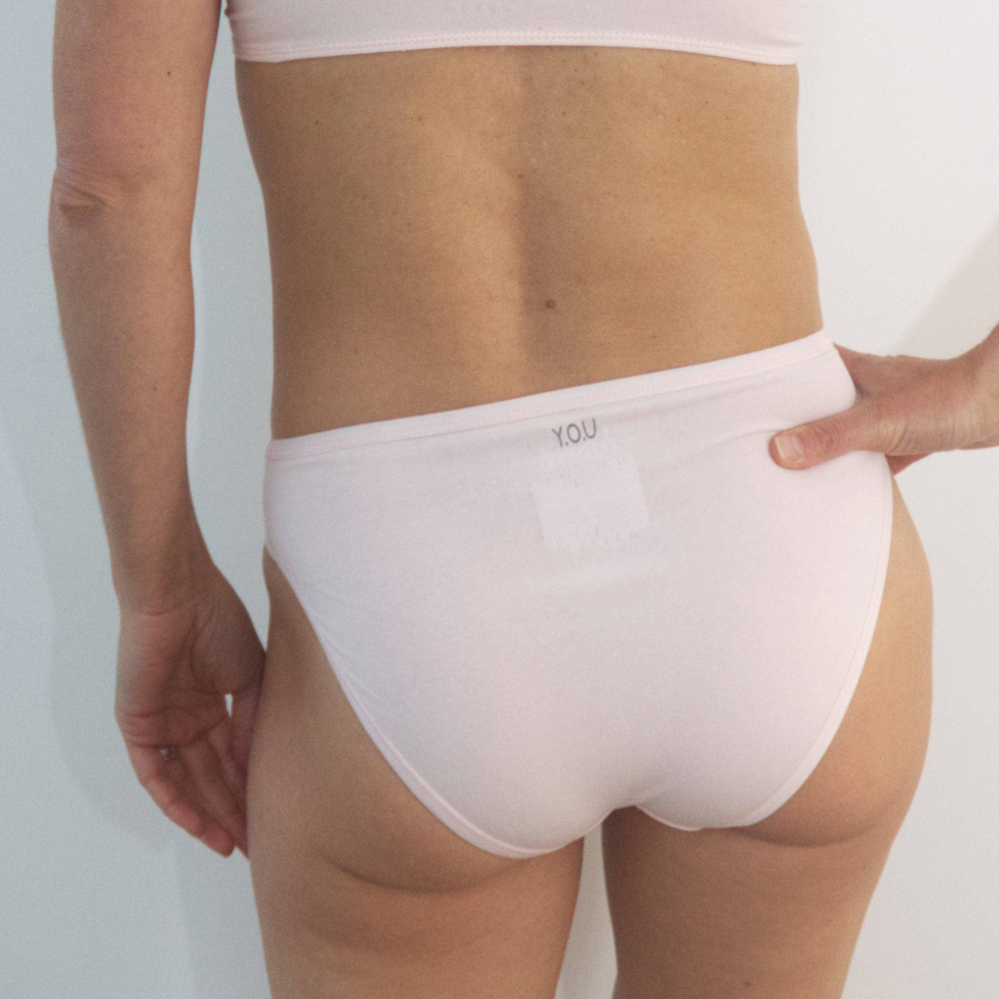 A woman wearing light pink, mid-rise bikini bottoms shown from behind