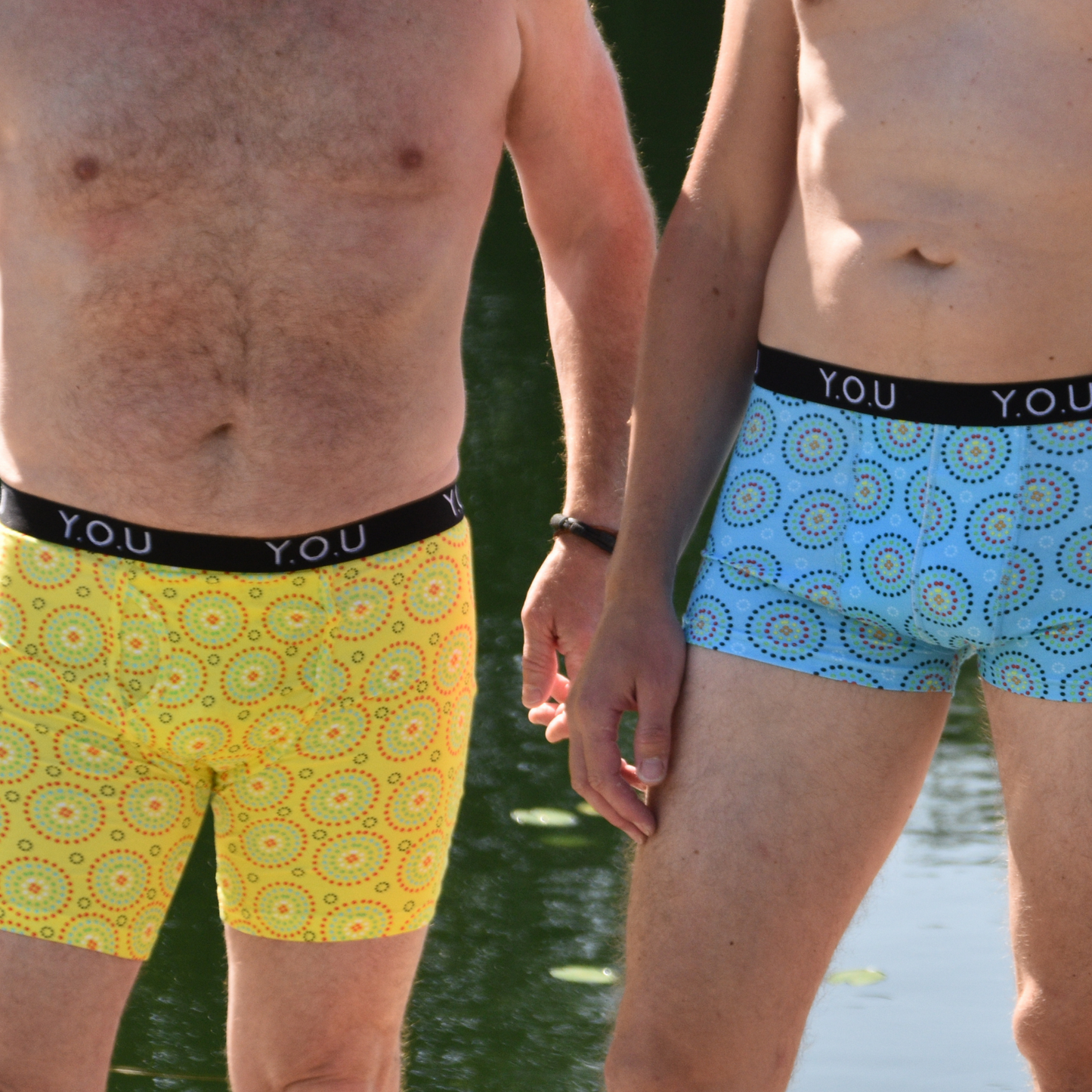 Men stand next to each other in front of a lake. One wears Blue Mara Short Trunks and the other wears long legged yellow mara trunks