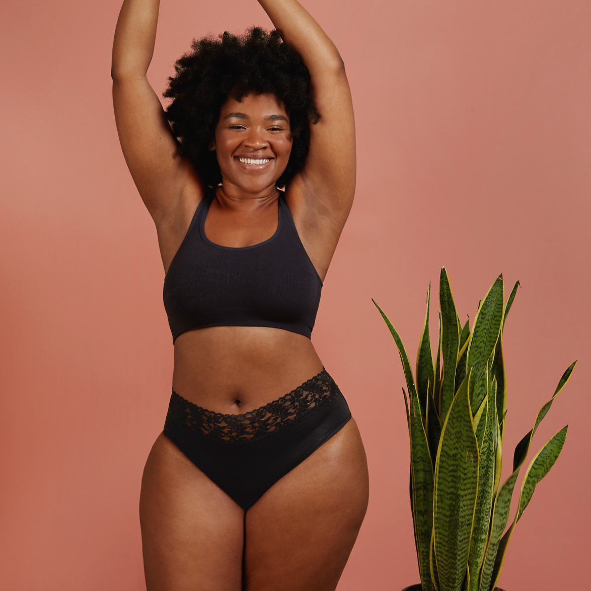 a woman wears a black period pant with lace and a black crop top with her hands in the air