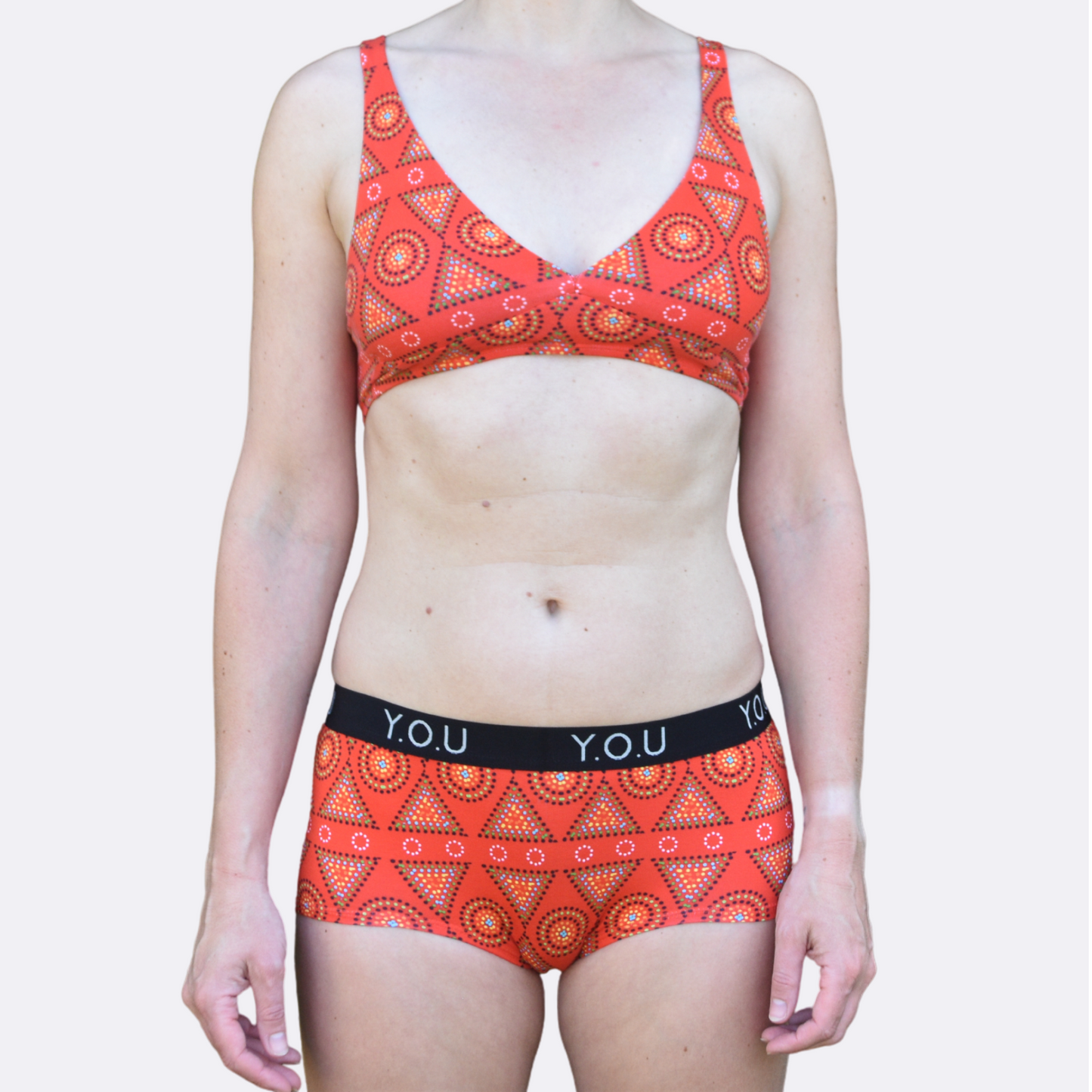 A light skinned woman wears our organic cotton Red Mara bralette and y.o.u branded boy shorts matching set - front view