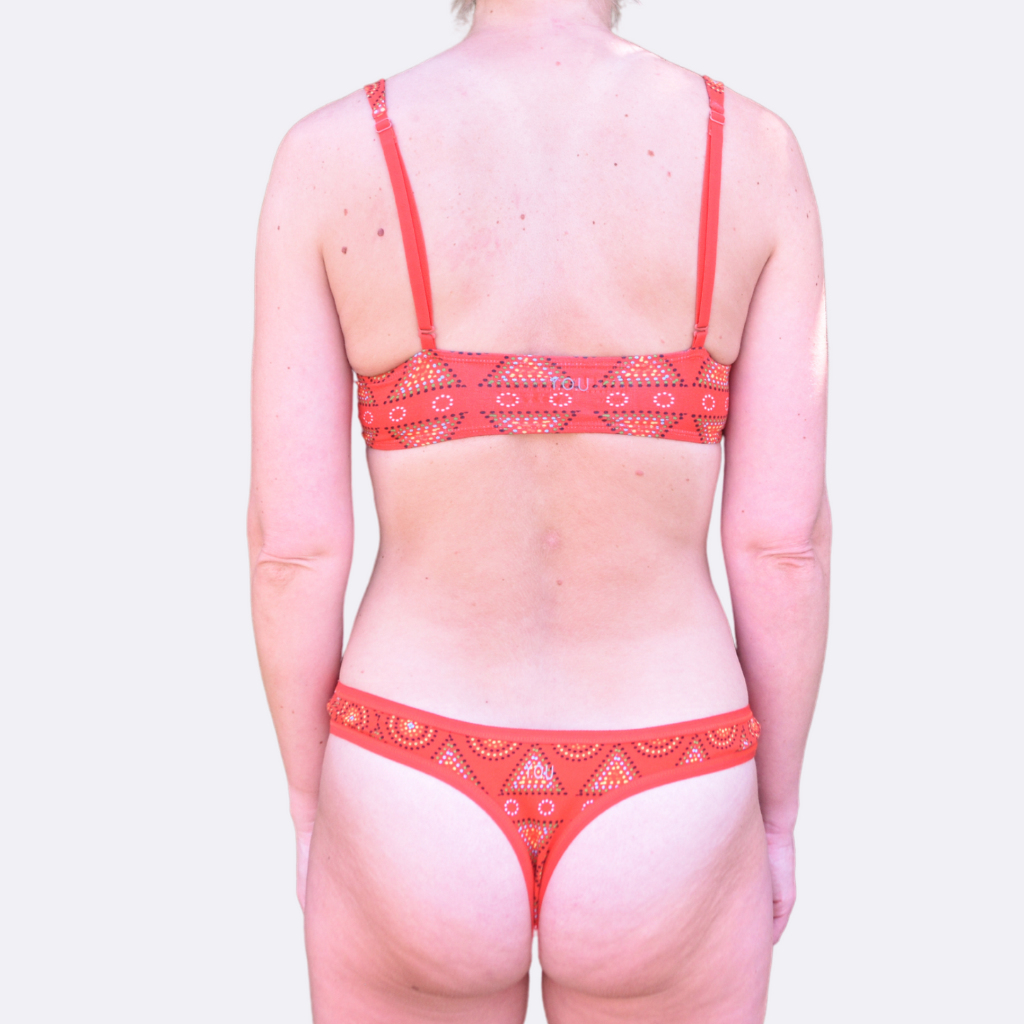 A light skinned woman wears an organic cotton red mara Bralettes and matching thong - back view