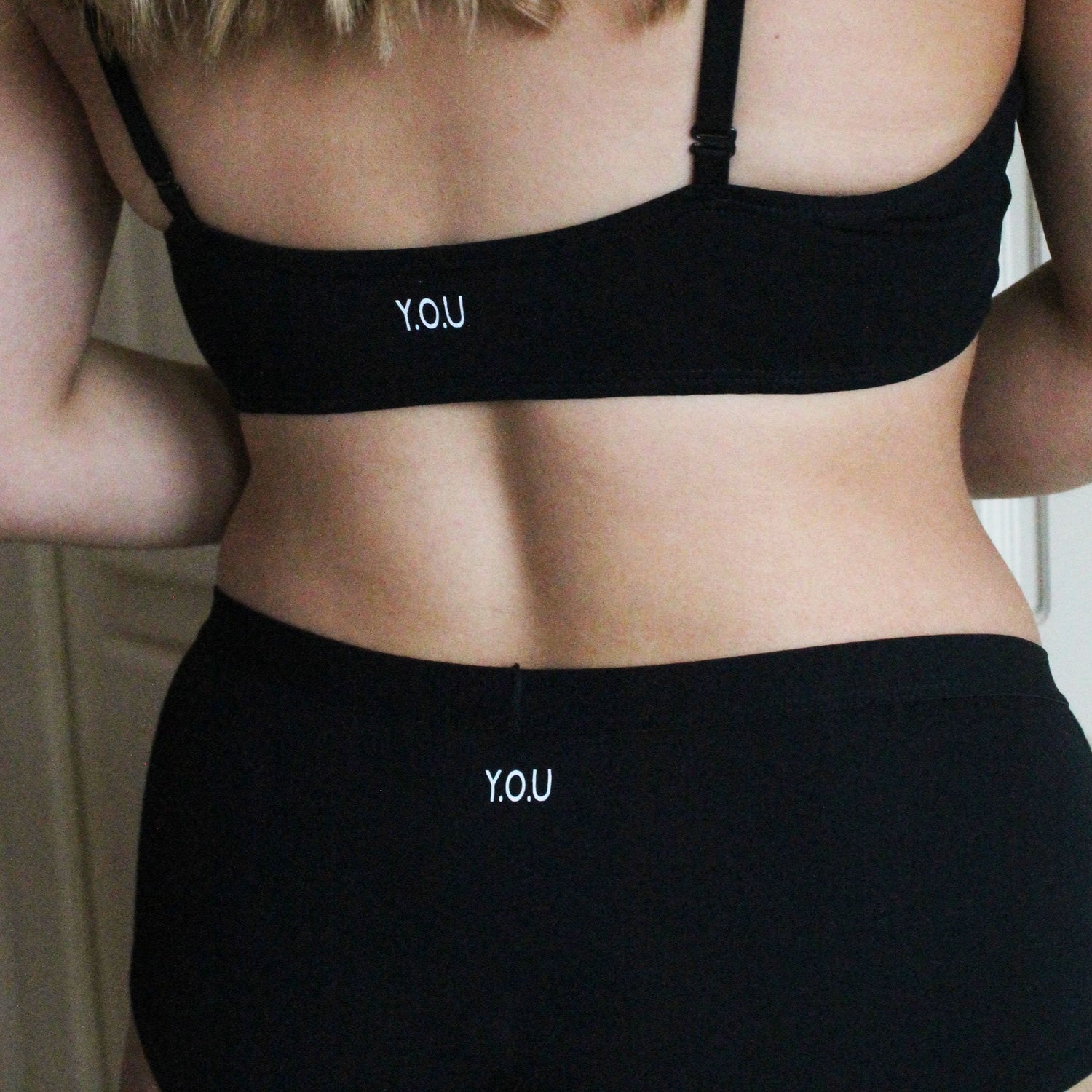 A woman wears a matching black bralette and by shorts set, facing away from the camera