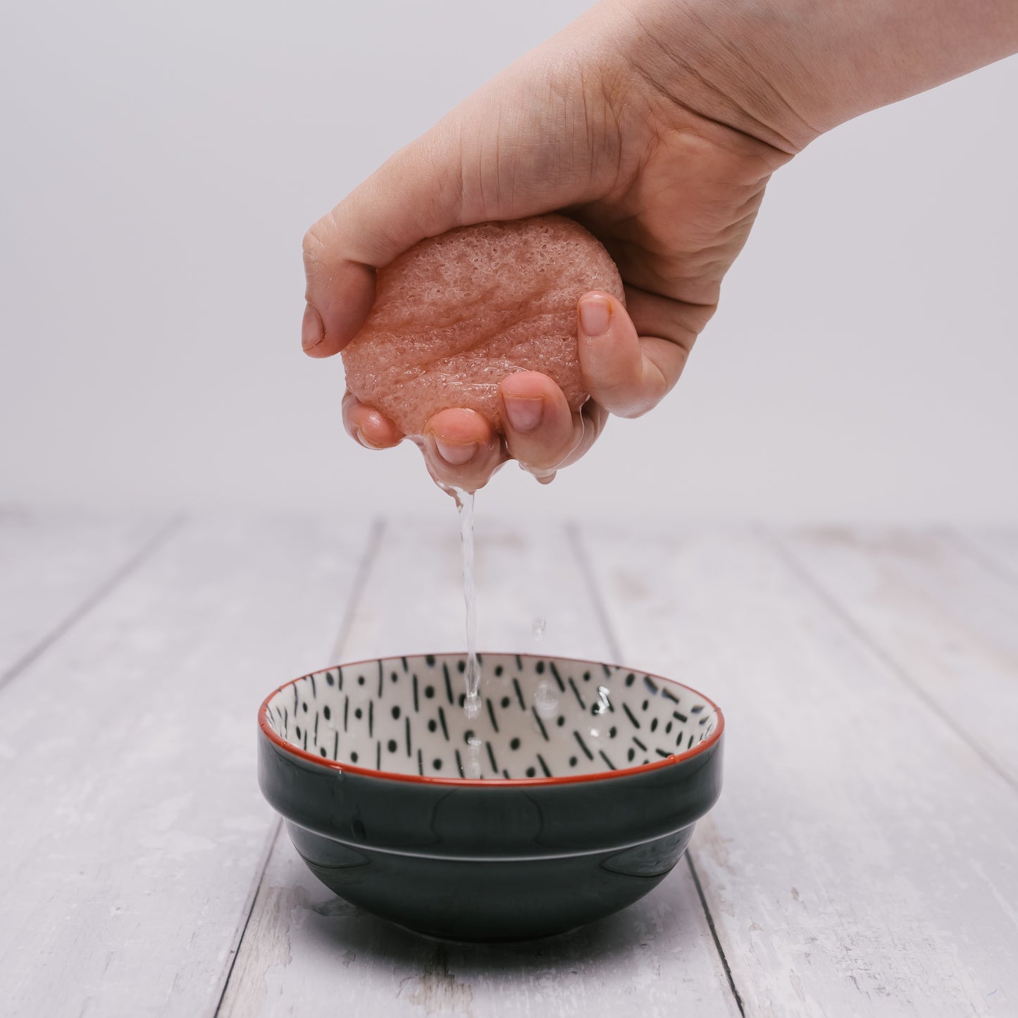 pale pink konjac sponge being wrung over a bowl